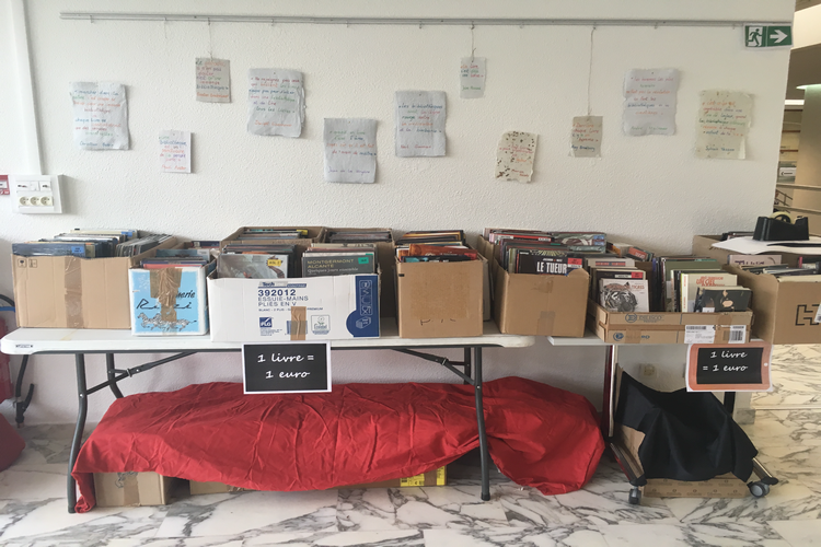 ensemble de cartons plein de libre posés sur des tables devant un mur blanc avec des affichettes