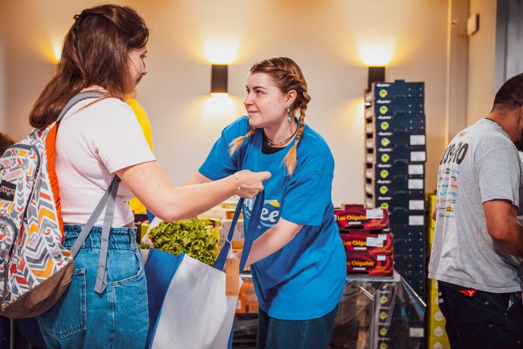 une jeune femme de l'association linkee met une salade dans le panier d'une étudiante lors d'une distribution alimentaire